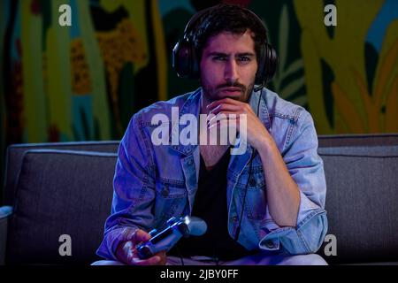Young man playing video game on couch in dark room Stock Photo