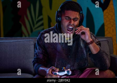Man screaming into headset microphone while playing video game. Stock Photo