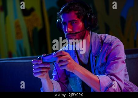 Concentrated young man playing video game while sitting on sofa at home Stock Photo