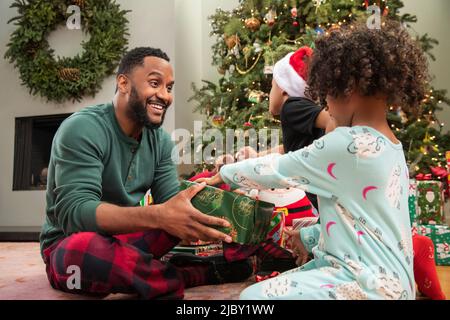 African American family unwrapping presents together sitting by Christmas tree Stock Photo