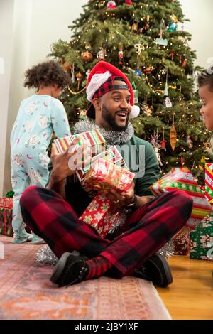 Kids piling up presents on theirs father's lap on Christmas Eve. Stock Photo