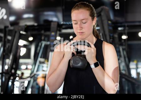 Woman in gym holding dumbbell doing squats Stock Photo