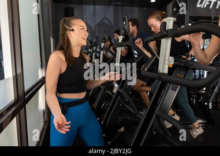 Young female workout instructor wearing a microphone headset encouraging her class while they run on treadmill Stock Photo