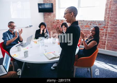 Happy young businesswoman receiving praise from her team during a meeting in an office. Successful young businesswoman smiling cheerfully while being Stock Photo