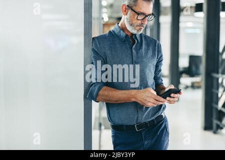 Creative businessman sending a text message in an office. Mature businessman using a smartphone to communicate with his clients. Experienced businessm Stock Photo