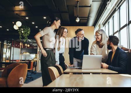 Smiling businesspeople having a discussion while collaborating on a new project in an office. Group of happy businesspeople using a laptop while worki Stock Photo