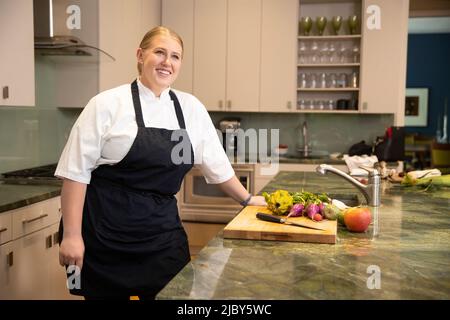 Portrait of Chef Megan Gill in kitchen looking up off camera, smiling. Stock Photo