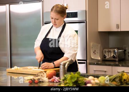 Professional Chef Megan Gill in kitchen looking down while cutting up vegetables. Stock Photo