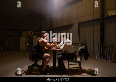 Two men preparing to have miss-matched arm wrestling contest in dingy warehouse Stock Photo