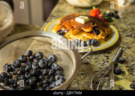 Detail of plate of pancakes with fruit on messy kitchen counter after making blueberry pancakes Stock Photo