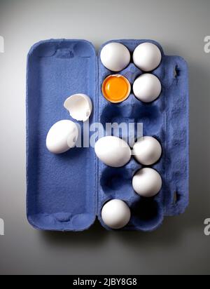 Aerial view of whole eggs and cracked egg showing yoke and broken shell in blue egg carton Stock Photo
