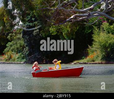 Boy rowing row boat and young sister flicking water at him from stern Stock Photo