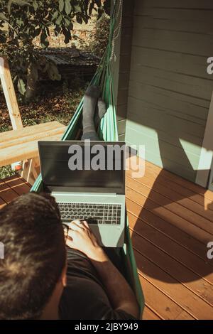 A top view of man working in hammock near cottage. Distant work, freelancer Stock Photo