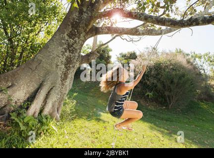 Teenage girl swinging on rope swing tied to big old tree Stock Photo