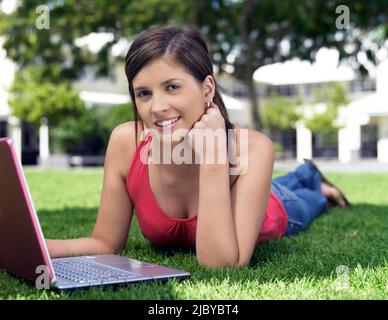 Female student lying on grass using her laptop computer Stock Photo