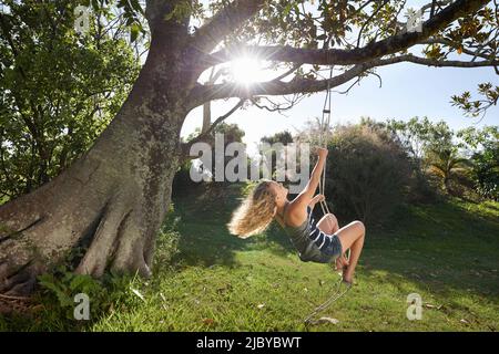 Teenage girl on a rope swing hanging from big old tree Stock Photo