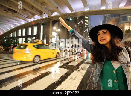 Beautiful Fashionable young woman hailing a taxi on 42nd Street outside Grand Central Station on a rainy stormy night, Manhattan, New York City, NY Stock Photo