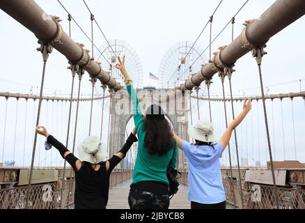 Mother and two young daughters happy for visiting the Brooklyn Bridge, hands raised showing victory sign - Manhattan, New York City, New York, USA Stock Photo