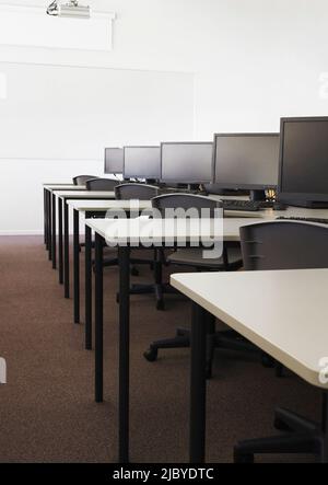 Row of computers on desks with chairs in empty room Stock Photo