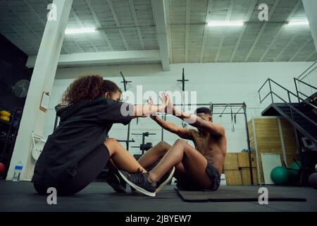 Mixed race friends doing cross fit in the gym. Male personal trainer giving African American female a high-five after exercising. High quality photo Stock Photo