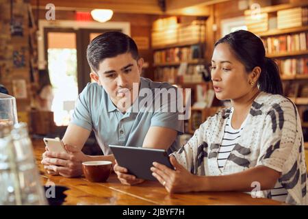 Young man and woman sitting at counter in cafe bookstore looking at tablet Stock Photo