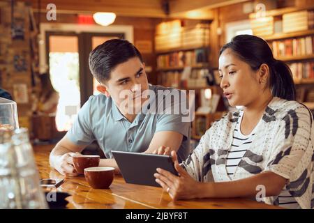 Young man and woman sitting at counter in cafe bookstore looking at tablet Stock Photo