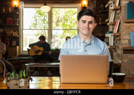 Portrait of young man sitting at table in coffee shop bookstore using laptop computer Stock Photo