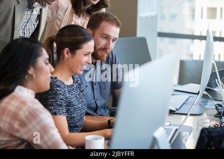 Young woman using laptop computer in conference room showing co-workers something on screen Stock Photo