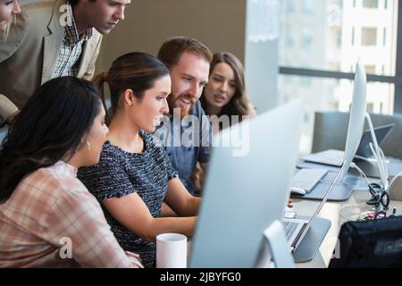 Young woman using laptop computer in conference room showing co-workers something on screen Stock Photo