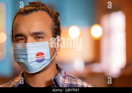 Indoor portrait of a Hispanic male wearing a mask and an I Voted Today sticker on the mask Stock Photo