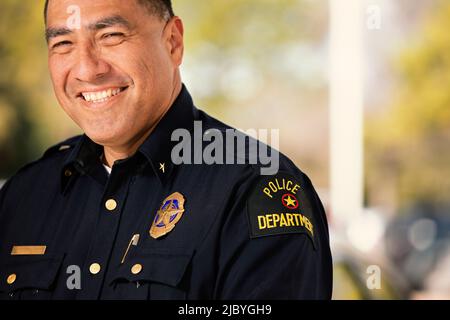 Portrait of Police officer standing outside with arms crossed looking towards camera smiling Stock Photo
