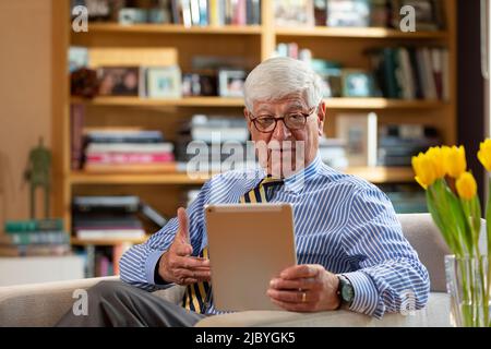 Senior Caucasian doctor practicing tele-medicine from his home office, Talking to patient via video call on tablet Stock Photo