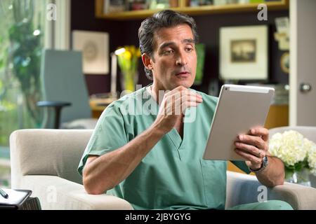 Hispanic Male doctor practicing tele-medicine from his home office, Talking to patient via video call on tablet Stock Photo