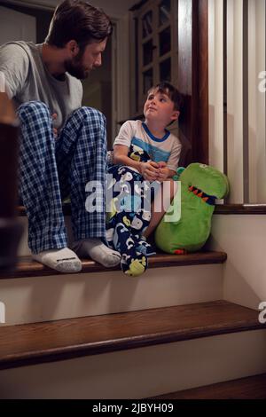 Father and son sitting at top of stairs in home getting ready for bedtime Stock Photo