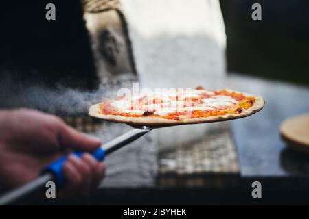 The pizza is ready and taken out of the wood-fired oven. The process of making homemade pizza. The concept of homemade fast food. Front view. Stock Photo