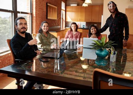 group of co-workers sitting at large conference table with their devices having discussion Stock Photo