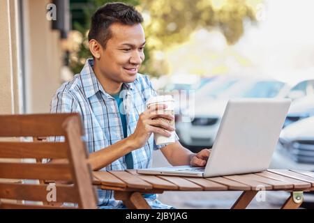 Malaysian man drinking coffee and using laptop at cafe Stock Photo