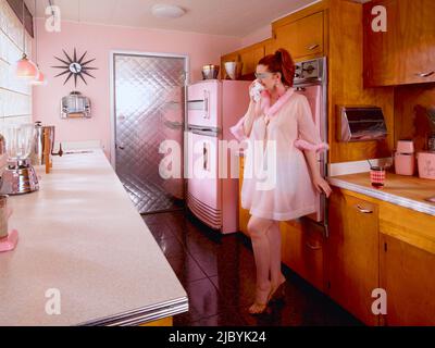 https://l450v.alamy.com/450v/2jbyk24/vintage-styled-portrait-of-a-woman-wearing-a-pink-nightgown-wiping-her-tears-away-in-a-mid-century-kitchen-2jbyk24.jpg