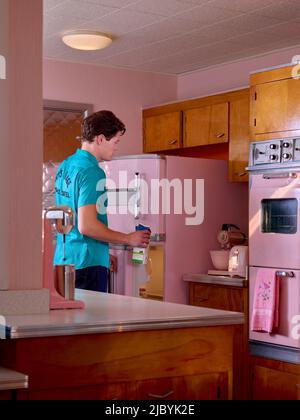 Vintage styled portrait of a man taking out milk from fridge in a pink mid century kitchen. Stock Photo