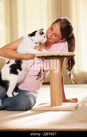 Portrait of teenage caucasian girl sitting on rug in living room showing new scratching post to her pet cat Stock Photo