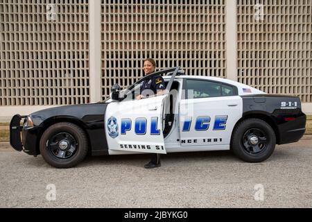 Policewoman standing in door of Police car looking towards camera smiling Stock Photo