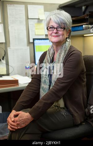 Portrait of woman sitting at her desk in office building with hands clasped on knees, looking at camera smiling Stock Photo