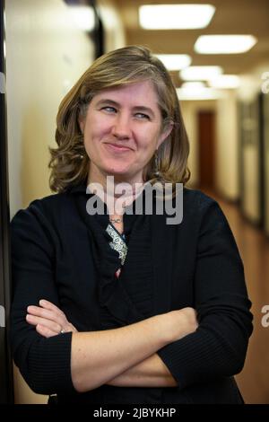 Portrait of middle aged woman with arms crossed in hallway of office building, smirking looking off camera Stock Photo