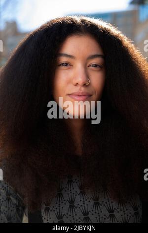 Portrait of woman with long hair standing outside, looking at camera Stock Photo