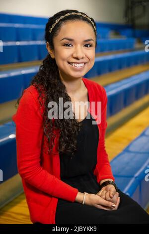 Smiling portrait of young ethnic woman sitting on bleachers in gymnasium Stock Photo