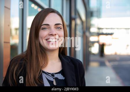 Portrait of woman with long hair standing outside in open shade, smiling looking at camera Stock Photo