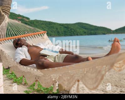 Hispanic man sleeping in hammock at beach Stock Photo