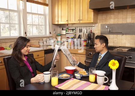 Couple reading newspapers in kitchen Stock Photo