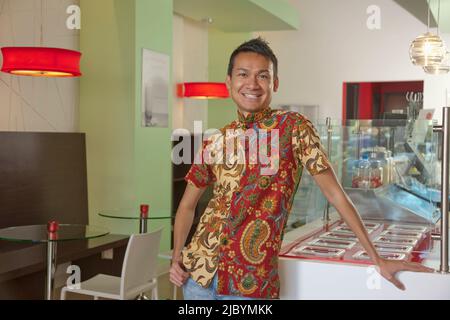 Smiling Malaysian man standing in cafe Stock Photo