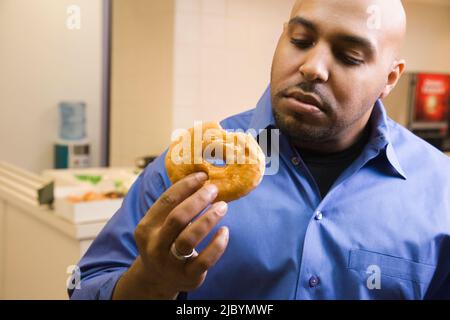 Mixed race businessman eating donut in office Stock Photo